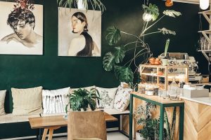 Stylish café interior featuring modern décor, green walls, plants, and comfortable seating.