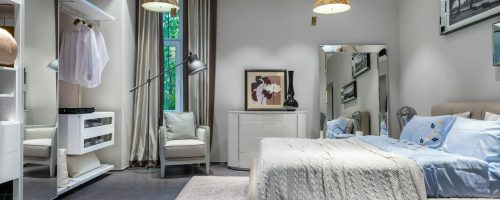 Comfortable bedroom with knitted coverlet and cushions built in spacious wardrobe armchair chest and mirror and hanging lamps