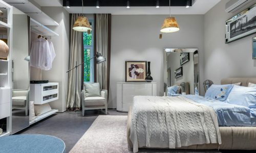 Comfortable bedroom with knitted coverlet and cushions built in spacious wardrobe armchair chest and mirror and hanging lamps